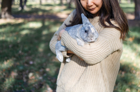 Adorable young rabbit and woman sit together outdoors in autumn forest. Asian woman wear warm sweater with pet in relax and calm.の写真素材