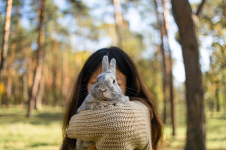 Adorable young rabbit and woman sit together outdoors in autumn forest. Asian woman wear warm sweater with pet in relax and calm.の写真素材