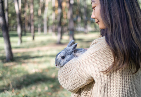 Adorable young rabbit and woman sit together outdoors in autumn forest. Asian woman wear warm sweater with pet in relax and calm.の写真素材
