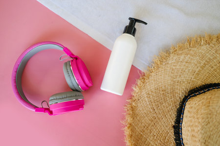 Summer vacation items and accessories. suntan cream, headphones and sun hat on pink background. Top...