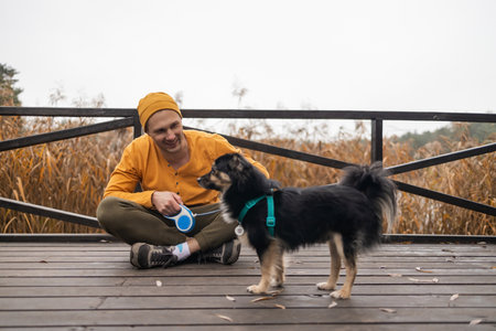 handsome bearded man in yellow hat embracing his dog in autumn park.