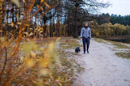 Bearded man in funny hat on autumn walk with dog in evening forest.