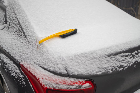 cleaning snow from car windshield outdoors on winter day.