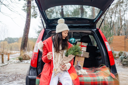 Happy Asian girl in white sweater playing with Christmas bunny in car trunk.の写真素材
