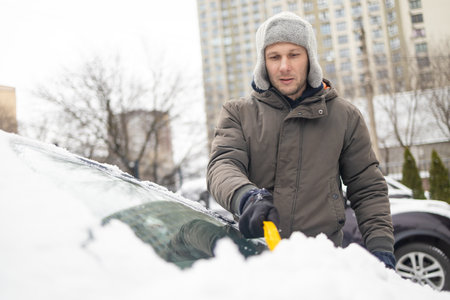 Transport, winter, weather, people and vehicle concept - man cleaning snow from car with brushの写真素材