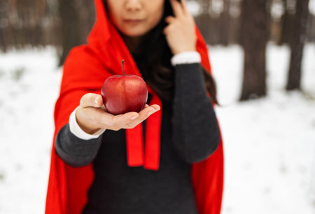 Red Hooded Woman Holding an Apple Fairytale Portrait - Fairytale image of a beautiful girl in a red hood near the forestの写真素材