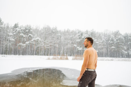 Young man standing by ice hole and ready to swim in the winter waterの写真素材