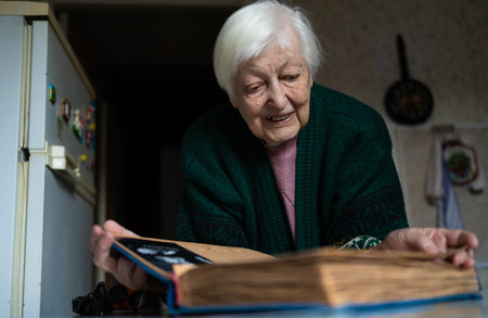 Cheerful senior female holding family photo album sitting at home. nostalgia concept and memory of old times.の写真素材