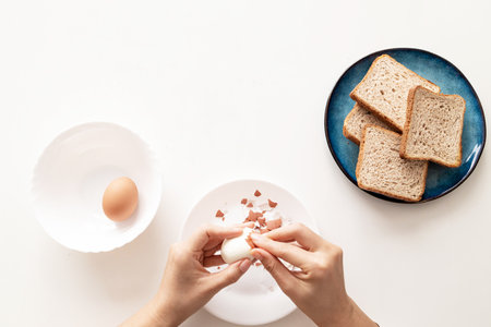 Woman peeling boiled egg on white table.