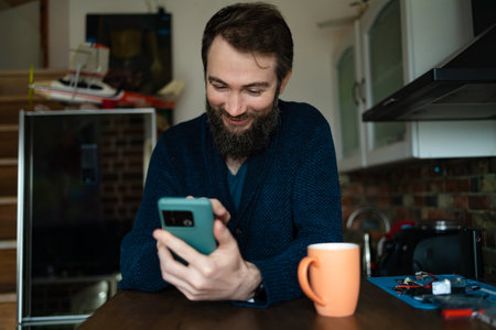 Shot of a handsome young man drinking coffee at home. Happy man drinking a cup of coffee at home. Shot of a young man using a smartphone and having coffee in the kitchen at home.の写真素材
