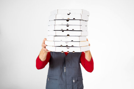 Photo of happy delivery man in red t-shirt and cap giving food order and holding many pizza boxes isolated on white backgroundの写真素材