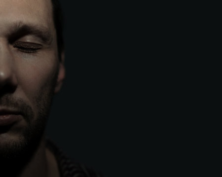 Ukrainian man with serious face and eyes closed in the dark.