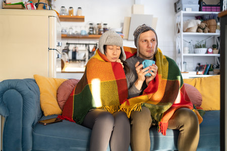 Couple cold on sofa at home with winter coat in a blanket.の写真素材