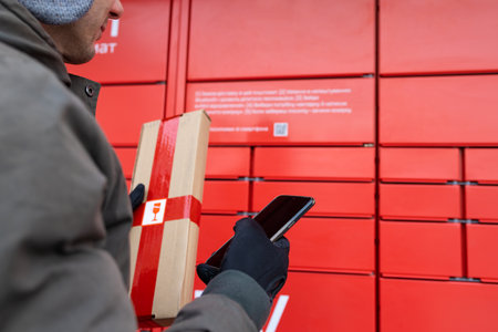 A man with a box in his hands near the self-service mail terminal. Parcel delivery machine. Person holding a cardboard box. Mail delivery and post service, online shopping, e-commeの写真素材
