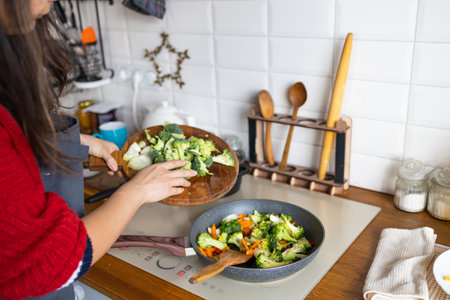 Woman cooking frying fresh healthy vegetables on pan on induction stove. lifestyle background.の写真素材