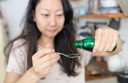healthcare, people and medicine concept - Asian woman pouring medicine or antipyretic syrup from...