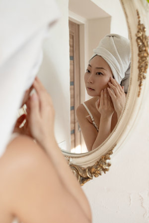 Portrait sad Asian middle aged woman looking in a mirror unhappy with wrinkles on her face. Skincare...