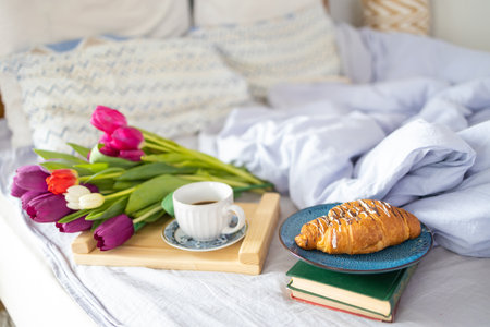 Breakfast served with love in bed, coffee, croissant and tulips on a tray on white bed linen at a romantic holiday morning, copy space, selected focusの写真素材