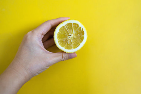 Hand holding fresh lemon slice on a yellow background.の写真素材