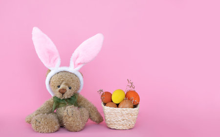 Easter eggs in the woven basket and bear toy isolated on pink background.の写真素材