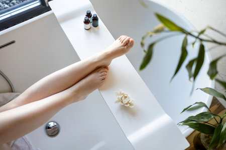 Young woman wearing bathrobe touching legs soft smooth skin applying lotion doing body care morning routine in bathroom. Spa, laser epilation hair removal, depilation. close upの写真素材