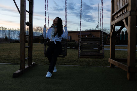 Young sad asian woman sitting on a swing in the evening.の写真素材