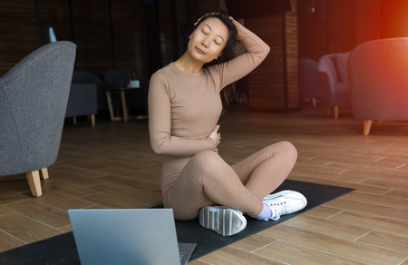 Attractive young asian woman doing yoga stretching yoga online at home. Self-isolation is profitable, fun and learning on the Internet. The concept of a healthy lifestyle.の写真素材