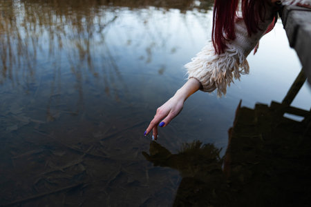 a woman's hand gently touches the water in the pond, a close horizontal photo on the theme of tranquilityの写真素材