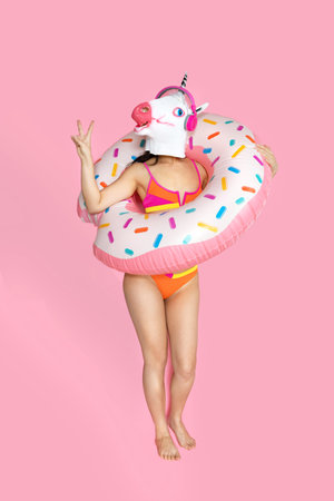 fun happy woman with slim body wear swimsuit and unicorn head hold pink inflatable ring isolated on...