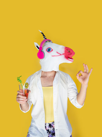 summer, vacation and people concept - happy young man in unicorn mask and headphones with juice cocktail dancing over yellow background.の写真素材