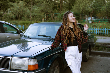 Millennial cool pretty girl with dreadlocks near car. Teen hipster girl smoking a marijuana...