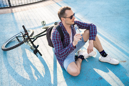 Young attractive man on a bicycle drink water.  Active healthy lifestyle. Sports man resting after exercise in nature.の写真素材