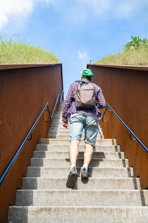 young unrecognizable man with backpack going up stairs a sunny day. Views from back and below.