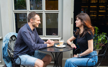 Happy smiling young dating couple having coffee together and enjoying life sitting at table in...