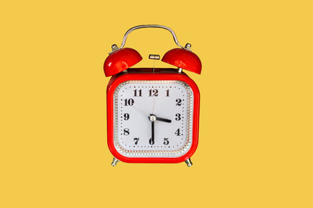Red vintage alarm clock on yellow colored background