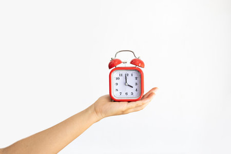 Time management, punctuality, awakening concept. Unrecognizable woman holds little red alarm clock in hand, shows how much time left, isolated on white wall.の写真素材