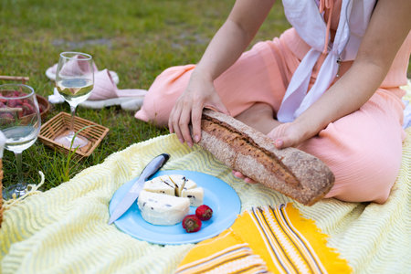 High angle of unrecognizable female cutting delicious cheese during picnic with strawberry in park.の写真素材