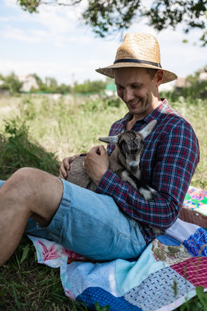 a happy man of Caucasian appearance, a farmer holds and hugs his favorite goat. a small goat. The...