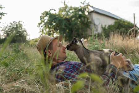 a happy man of Caucasian appearance, a farmer holds and hugs his favorite goat. a small goat. The concept of a summer countryside. Close to outdoor recreation.の写真素材