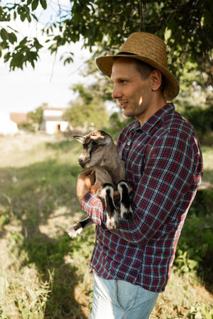 a happy man of Caucasian appearance, a farmer holds and hugs his favorite goat. a small goat. The concept of a summer countryside. Close to outdoor recreation.の写真素材