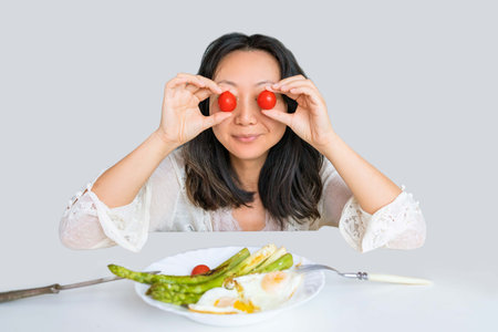 Young woman having breakfast with vegetables and eggs on a white background.の写真素材