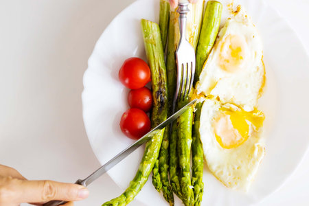 Fried eggs with asparagus and cherry tomatoes on white plate