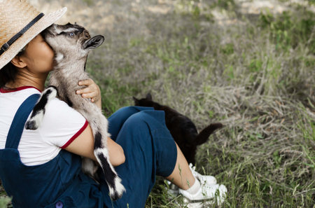 Young asian girl wearing a hat holding a goat in the field