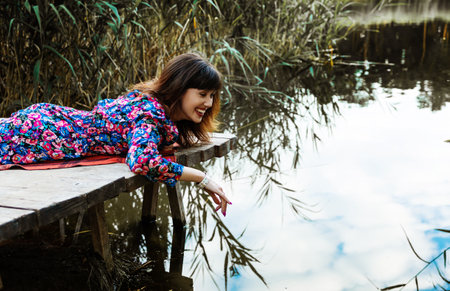 Young asian woman sitting on a wooden pier and looking at the lakeの写真素材