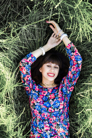 Portrait of a beautiful young brunette woman in a floral dress lying on the grass