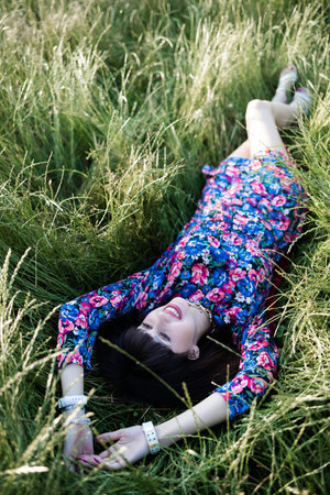 Young beautiful brunette woman in colorful dress lying down on green grassの写真素材