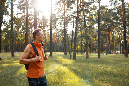 Handsome young man in orange t-shirt with backpack standing in the forest and looking awayの写真素材
