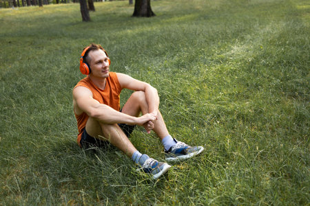 Young man listening to music with headphones while sitting on grass in parkの写真素材