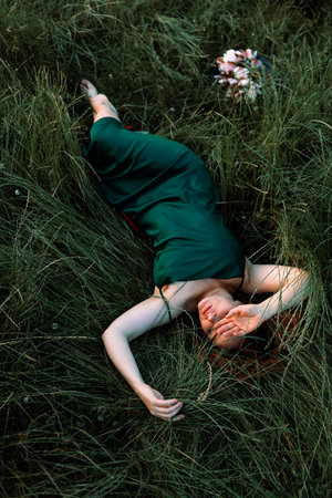 Young beautiful girl in a green dress lies on a green grass.の写真素材