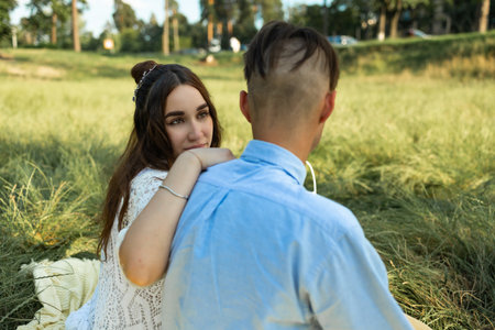 Young couple in love sitting on green grass in park and hugging.